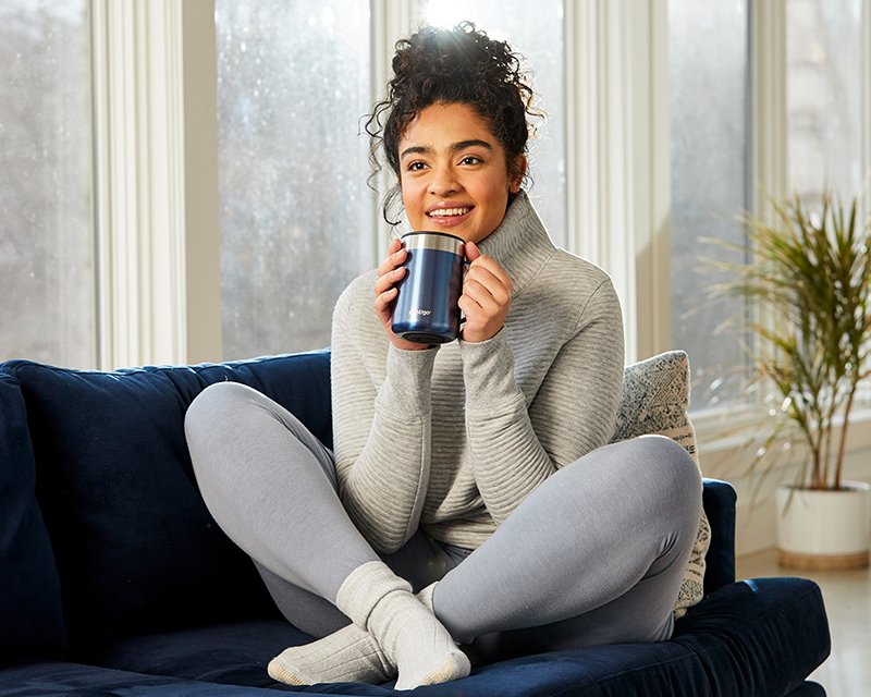 woman sitting on couch with travel mug